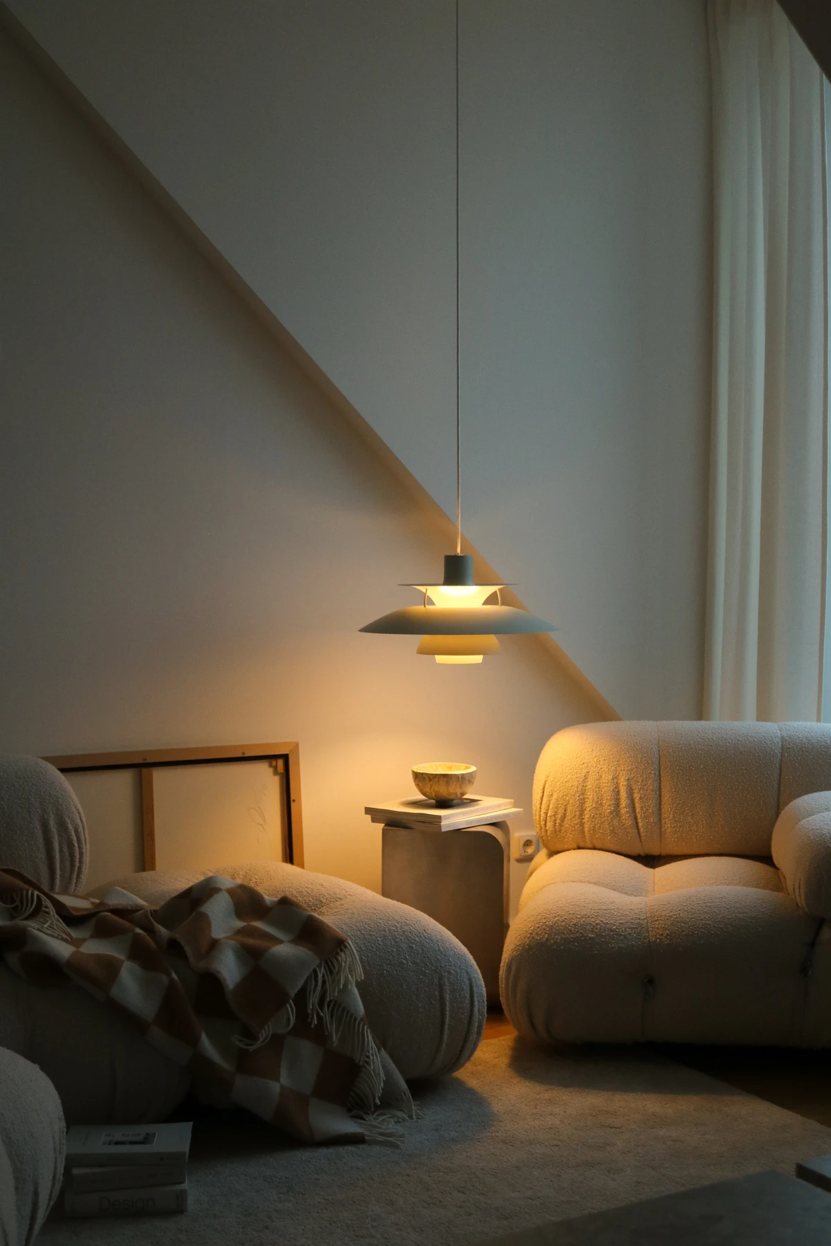 A PH 5 pendant casts a warm glow over soft lounge chairs in a quiet living room corner. © 2026 Louis Poulsen.