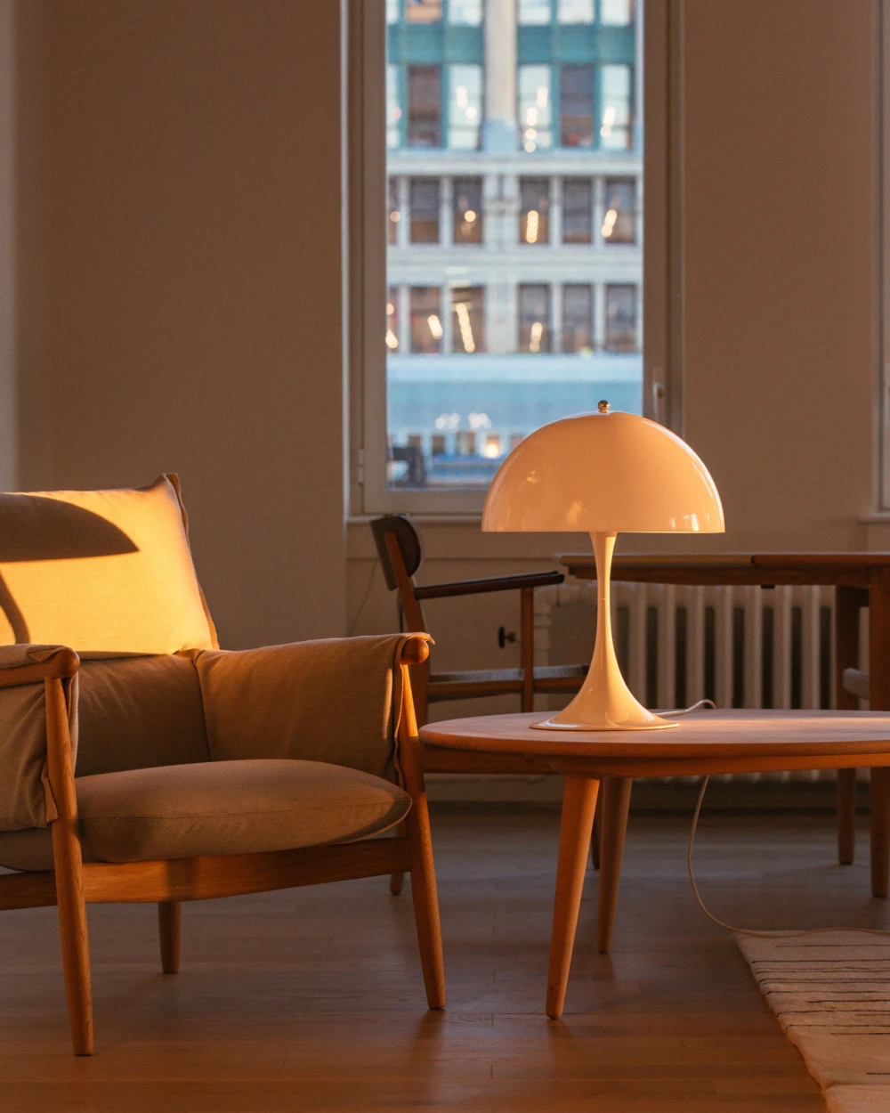 A Panthella 400 Table Lamp casts a warm glow on a wooden coffee table beside an armchair. © 2026 Louis Poulsen.