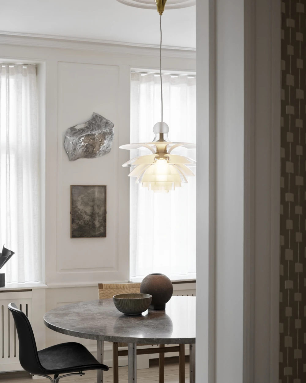 A PH Septima pendant in opal-white glass glows above a round marble table in a bright dining room. © 2026 Louis Poulsen.