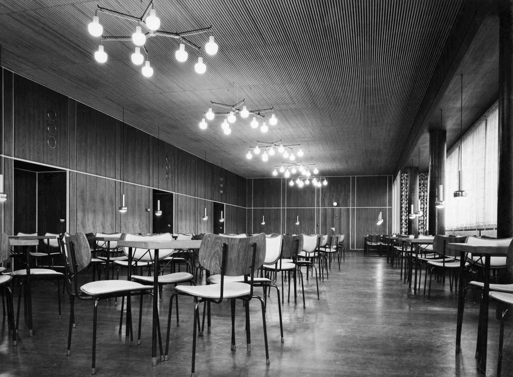 VL Ring Crown 3-5-7 Pendants light the large Folkets Hus hall, with rows of tables and chairs beside wood-panelled walls. © 2026 Louis Poulsen.