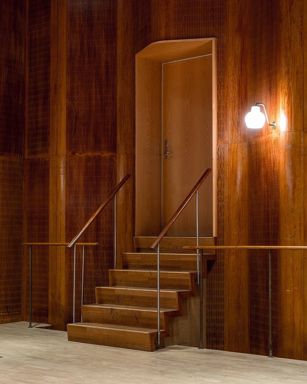 A PH 2/1 Wall Lamp in opal glass glows beside a wooden staircase in a richly timbered interior. © 2026 Louis Poulsen.