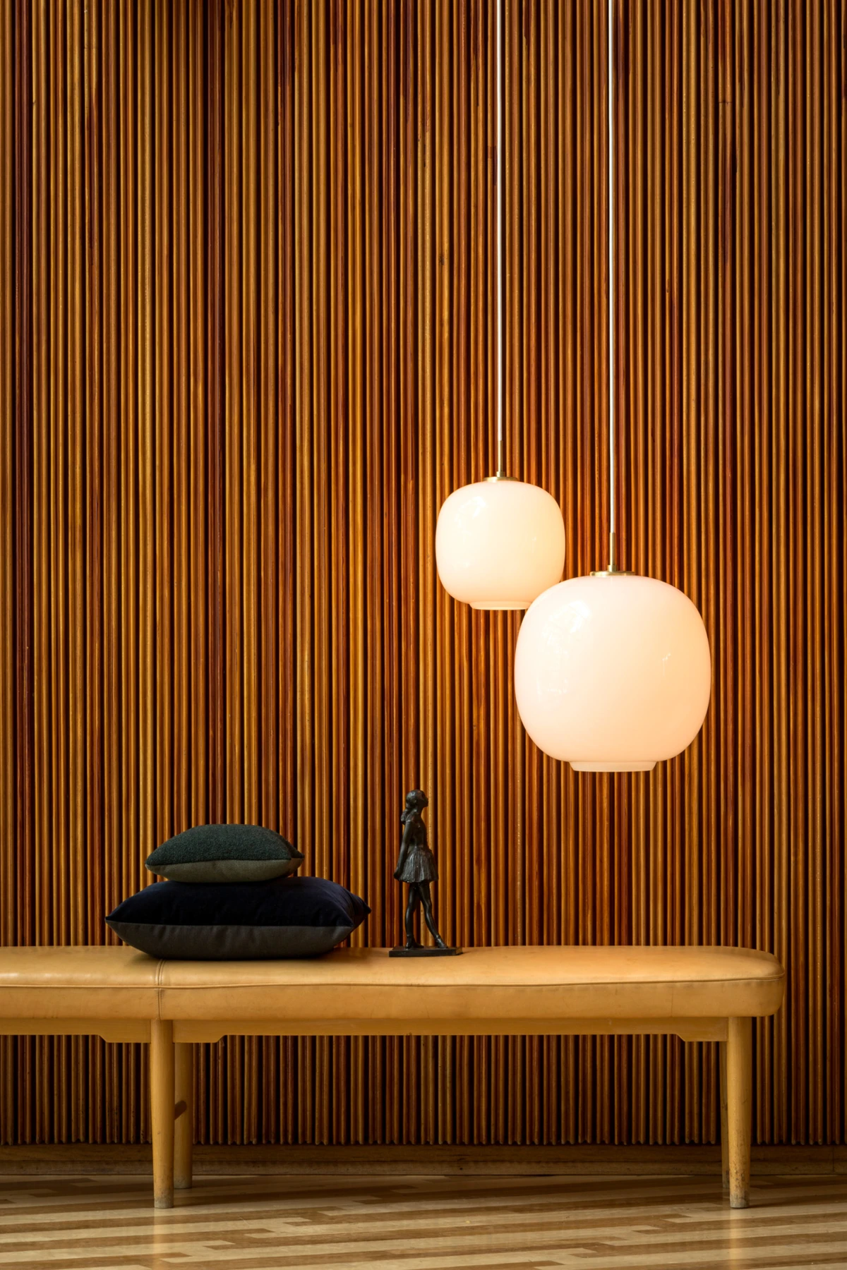 Two VL 45 Radiohus Pendants in opal glass glow above a bench against a wall of vertical wooden slats. © 2026 Louis Poulsen.
