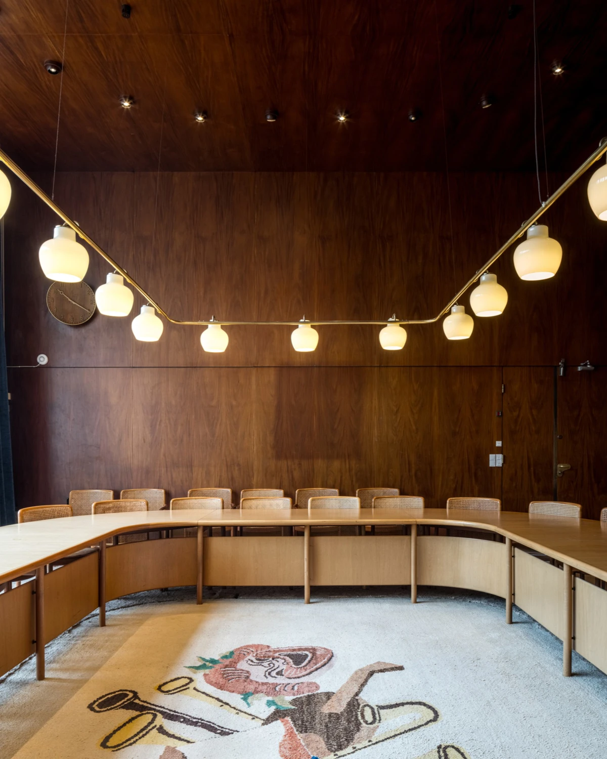 VL Ring Crown 3-5-7 Pendant with opal glass shades above a curved meeting table in a wood-panelled room. © 2026 Louis Poulsen.