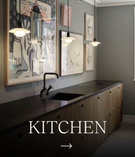 Two white PH 5 pendants hang above a dark kitchen counter with a sink and framed artwork. © 2026 Louis Poulsen.