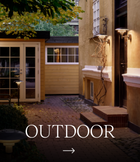 Brass Nyhavn Outdoor Wall Lamps illuminate a house facade in a leafy courtyard. © 2026 Louis Poulsen.