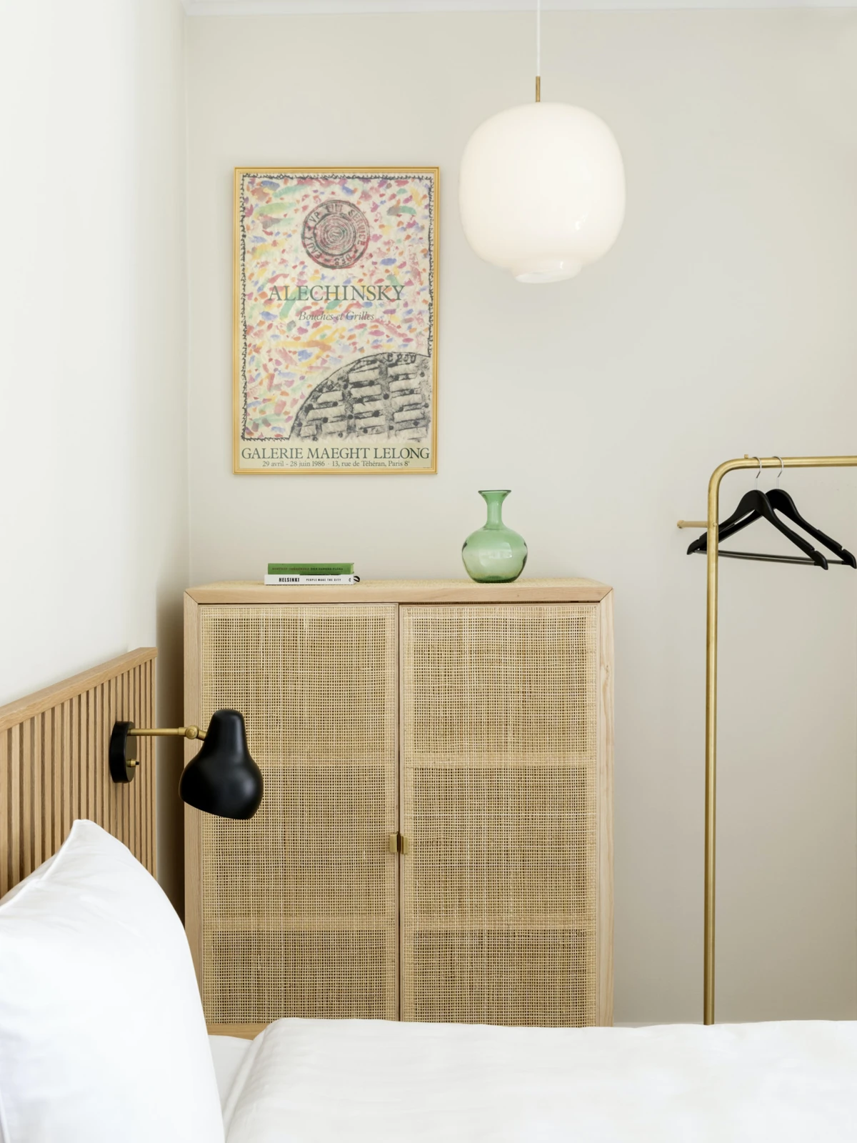 A white Moser Pendant and black AJ Wall Lamp in a bedroom with light wood and woven-cane furniture. © 2026 Louis Poulsen.