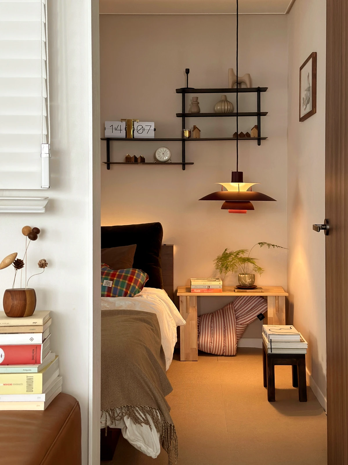 A dark PH 5 pendant casts a warm glow over a small bedside table in a calm bedroom. © 2026 Louis Poulsen.