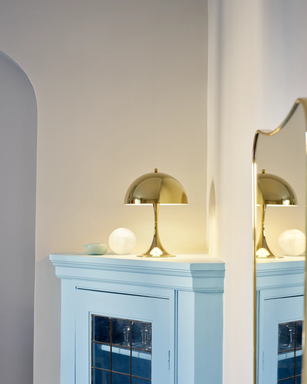 A brass-toned Panthella 320 Table Lamp casts a warm glow on a bedroom mantel. © 2026 Louis Poulsen.
