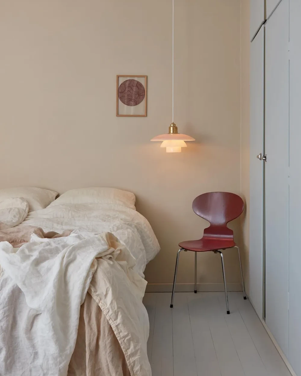 A PH 3½-3 Pale Rose Brass Pendant casts a warm glow over a bed in a calm bedroom with pale walls. © 2026 Louis Poulsen.