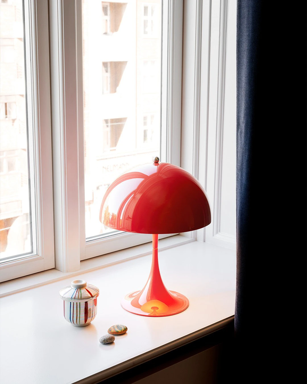 A coral Panthella 250 Table Lamp sits on a wide windowsill in a bright children's room. © 2026 Louis Poulsen.