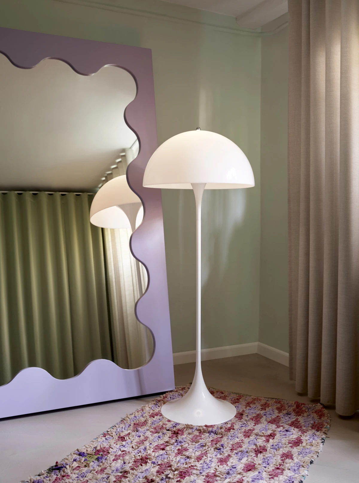A white Panthella Floor Lamp stands on a colourful rug beside a wavy mirror in a child’s room. © 2026 Louis Poulsen.