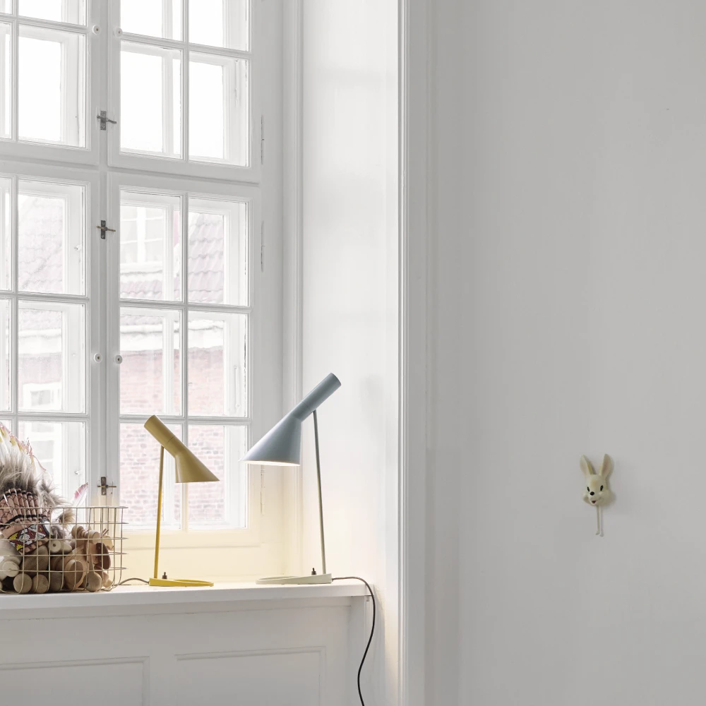 Yellow and pale grey AJ Table Lamps sit on a windowsill in a bright children's room. © 2026 Louis Poulsen.
