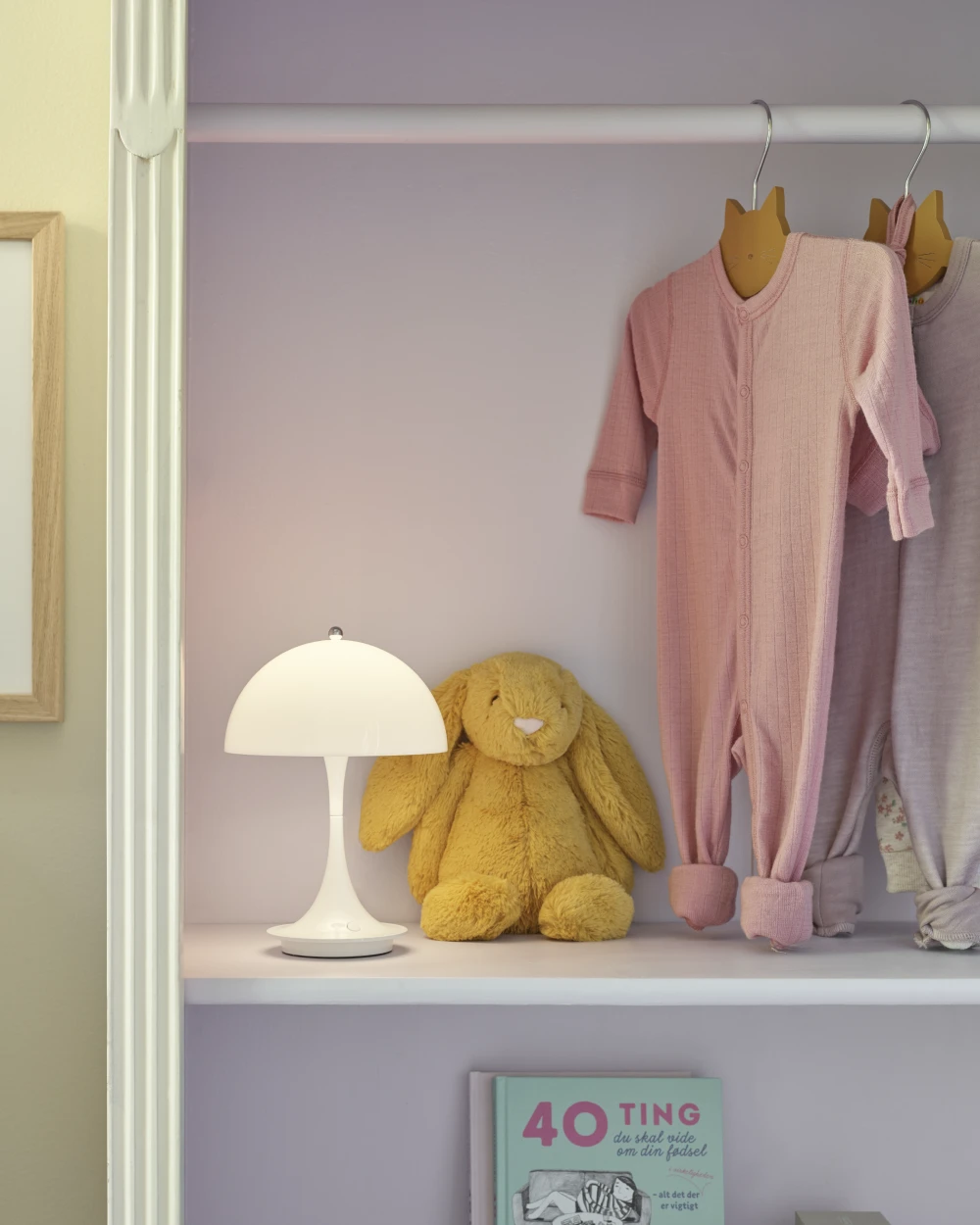 A white Panthella 250 Portable Lamp sits beside a plush rabbit and baby clothes on a shelf in a child’s room. © 2026 Louis Poulsen.