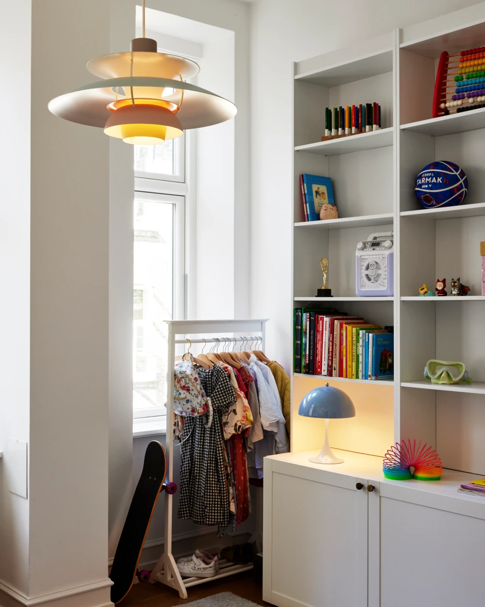 A PH 5 pendant and blue Panthella 250 Table Lamp light a bright child’s room with toys and books. © 2026 Louis Poulsen.