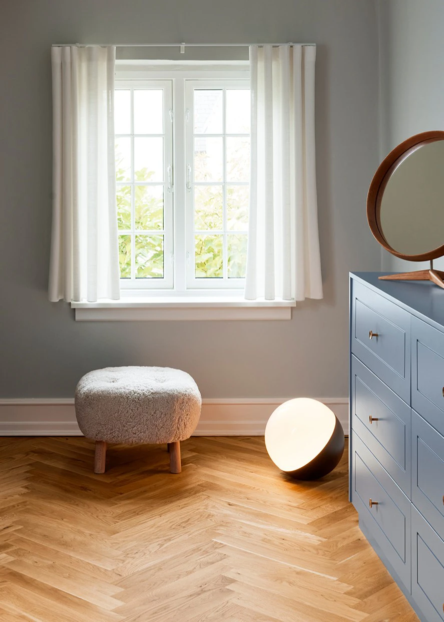 A black VL Studio Table/Floor Lamp glows on the wooden floor beside a blue dresser in a child’s room. © 2026 Louis Poulsen.