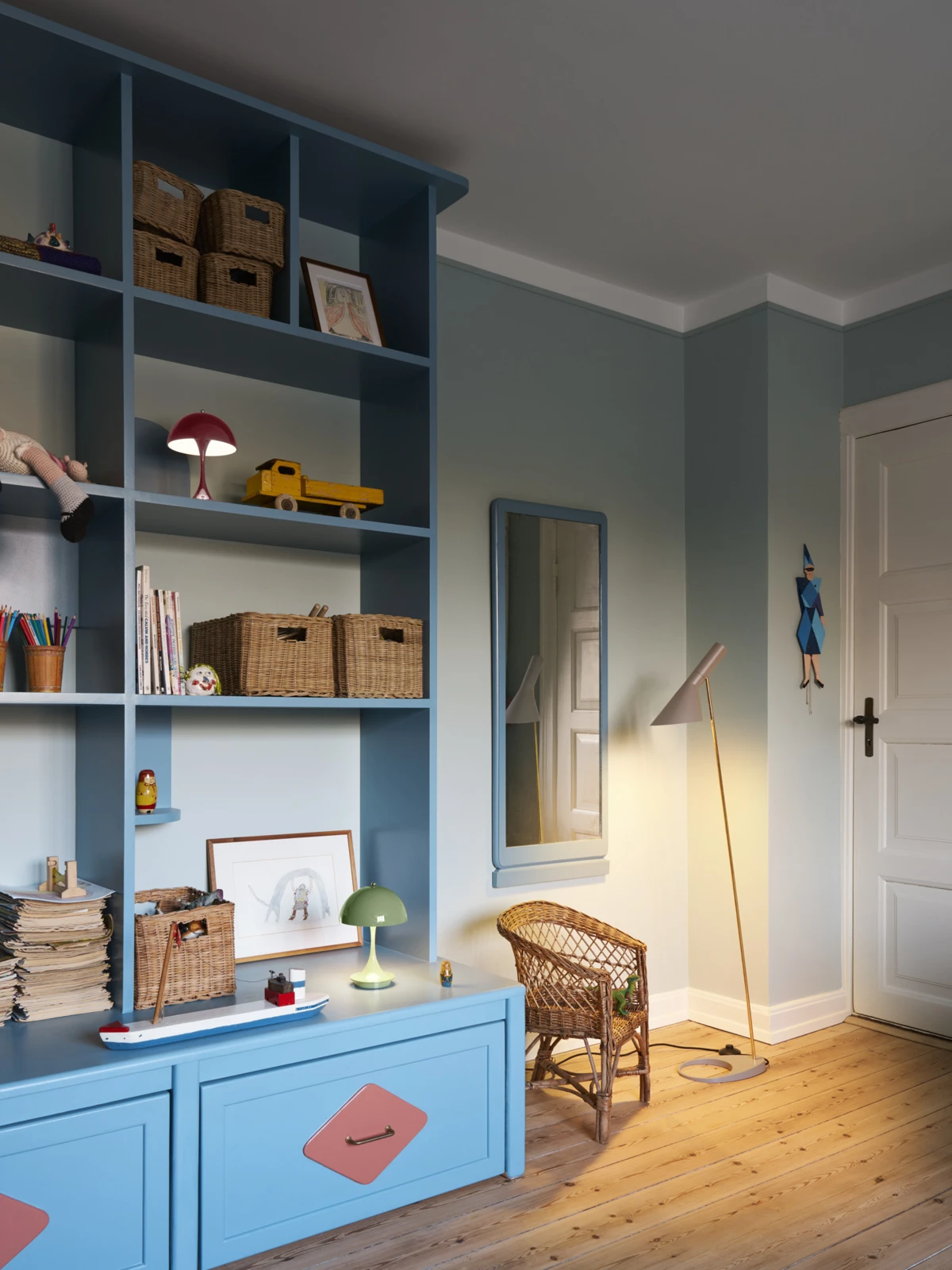 Red and green Panthella 160 Portable Lamps sit on shelves in a blue children’s room, with an AJ Floor Lamp beside a wicker chair. © 2026 Louis Poulsen.