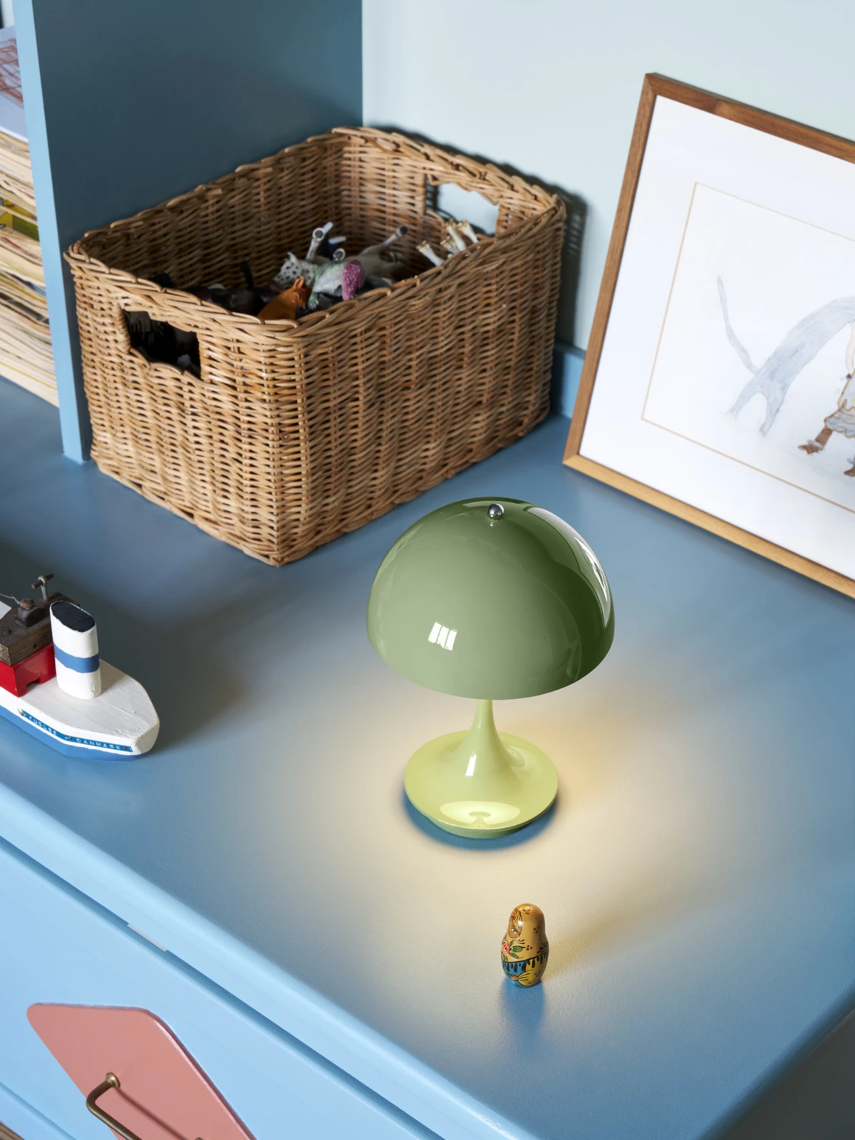 A green Panthella 160 Portable Lamp glows on a blue table in a child’s room beside toys and a wicker basket. © 2026 Louis Poulsen.
