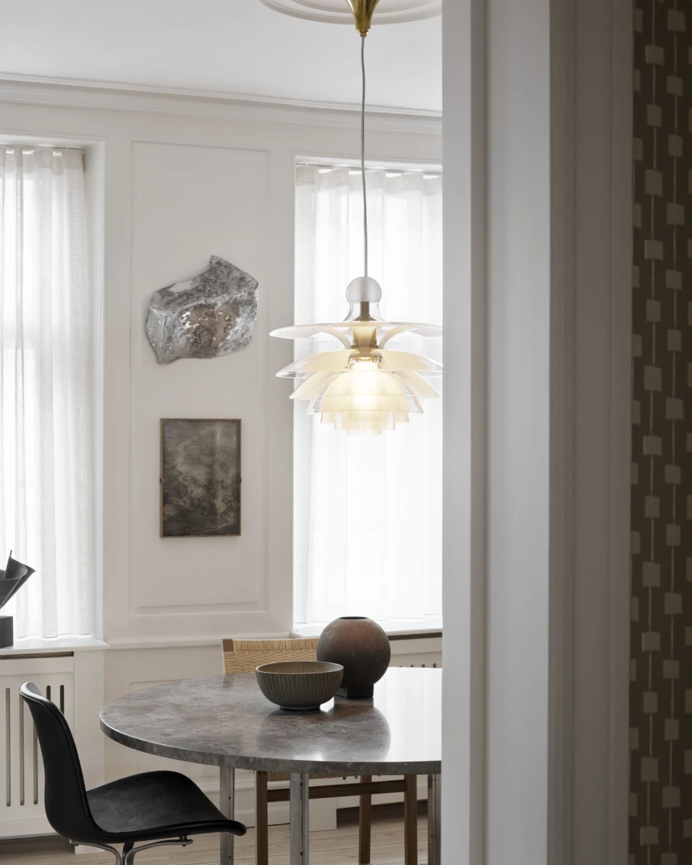 A white-glass PH Septima pendant glows above a round marble table in a bright dining room. © 2026 Louis Poulsen.
