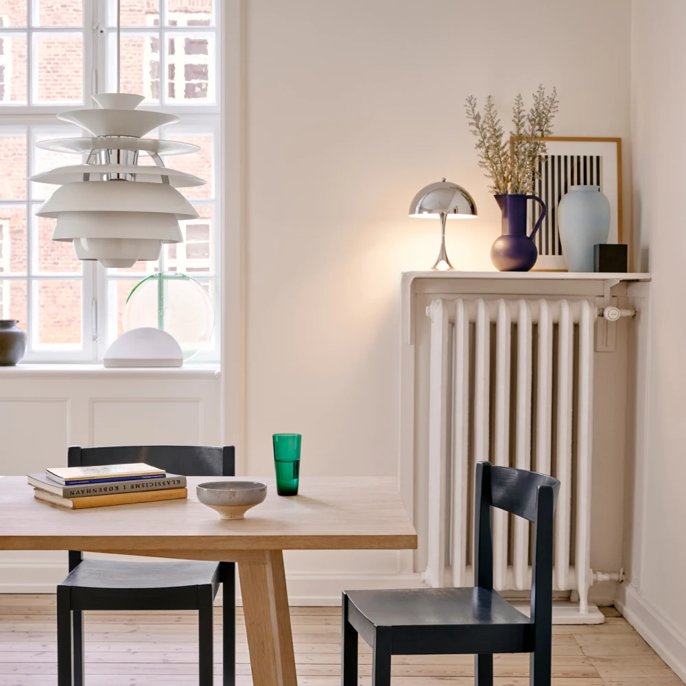 A white PH Snowball pendant hangs above a light wood dining table in a bright dining room. © 2026 Louis Poulsen.