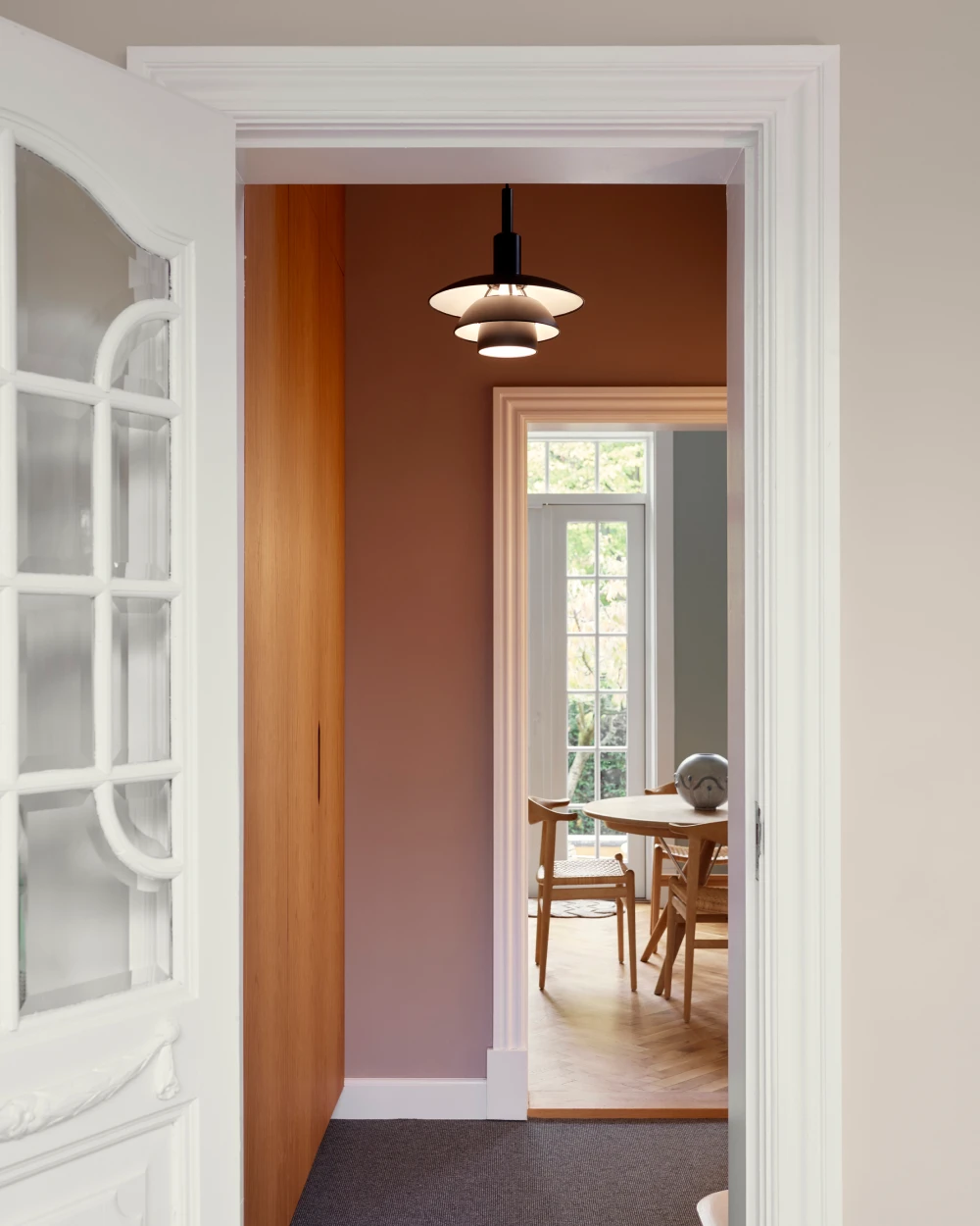 A black and white PH 5 pendant lights a hallway with terracotta walls and warm wood panelling. © 2026 Louis Poulsen.