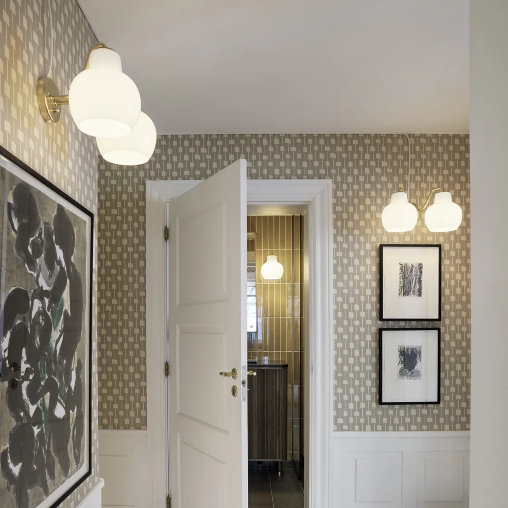 VL Ring Crown 2 Wall Lamps with opal-white shades light a patterned hallway with framed artwork. © 2026 Louis Poulsen.