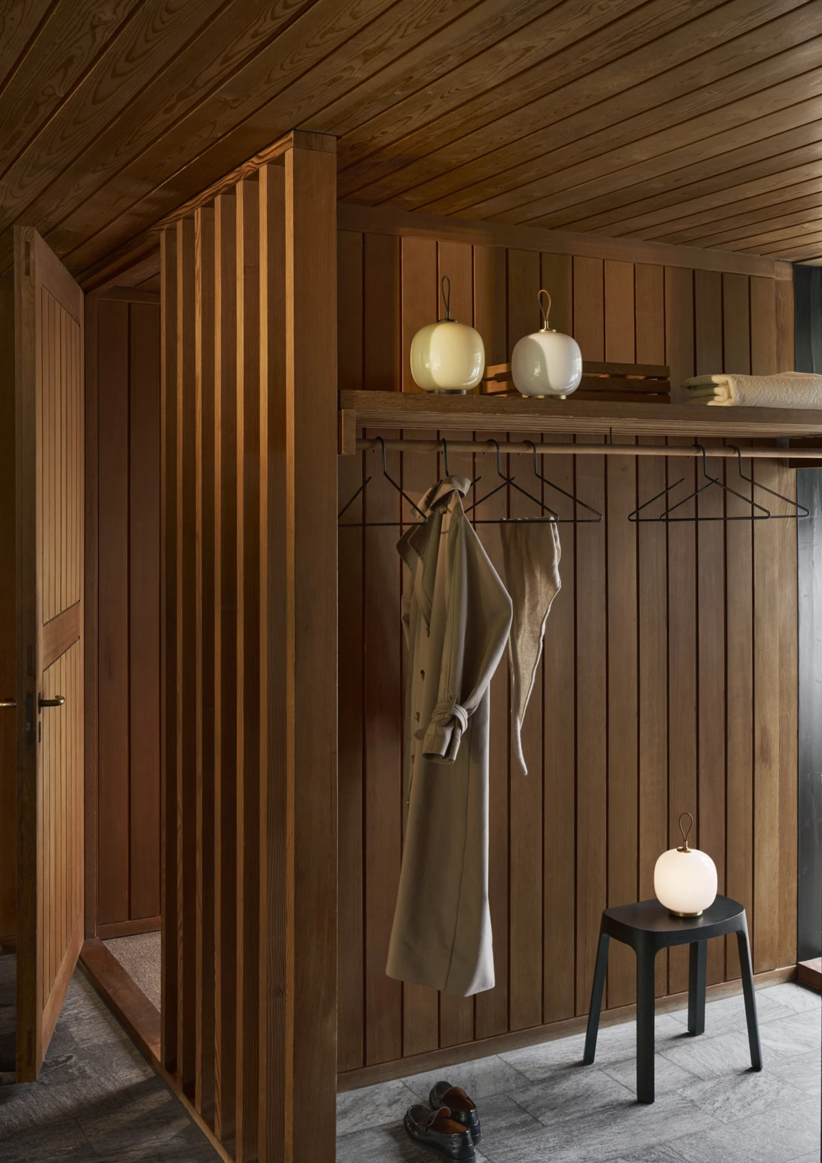 Three VL 45 Radiohus Portable Lamps in opal glass sit on a shelf and stool in a wood-panelled hallway. © 2026 Louis Poulsen.