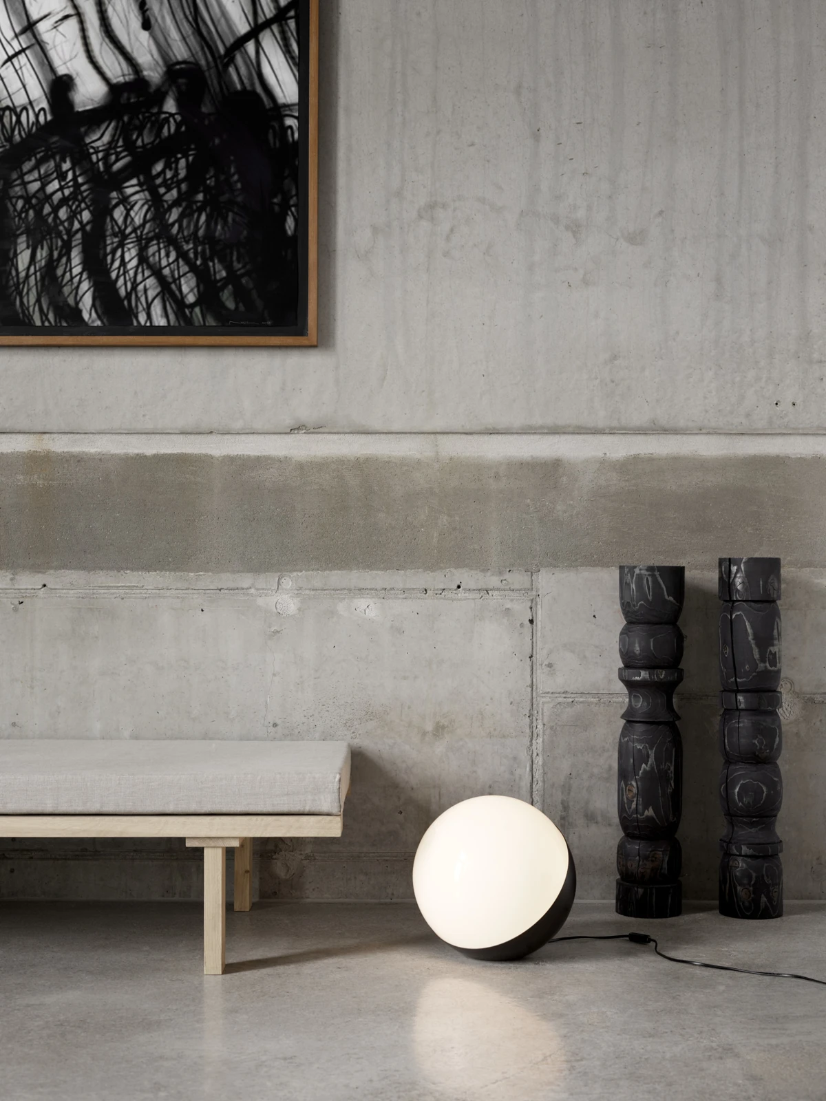 A black VL Studio Table/Floor Lamp with an opal glass shade stands on a concrete floor beside a bench. © 2026 Louis Poulsen.