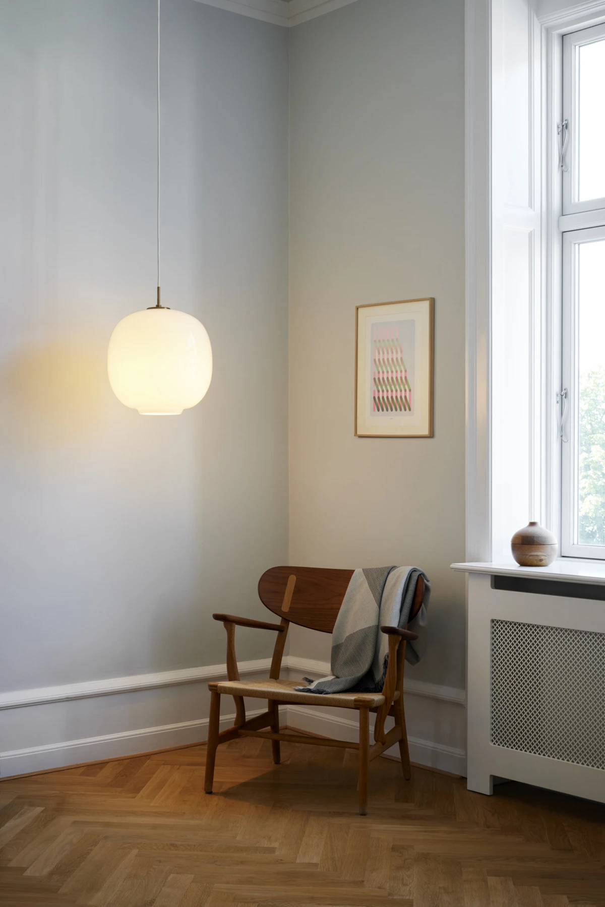 Een opaalwitte VL 45 Radiohus hanglamp verlicht een houten stoel in een rustige thuiswerkplek met parketvloer. © 2026 Louis Poulsen.