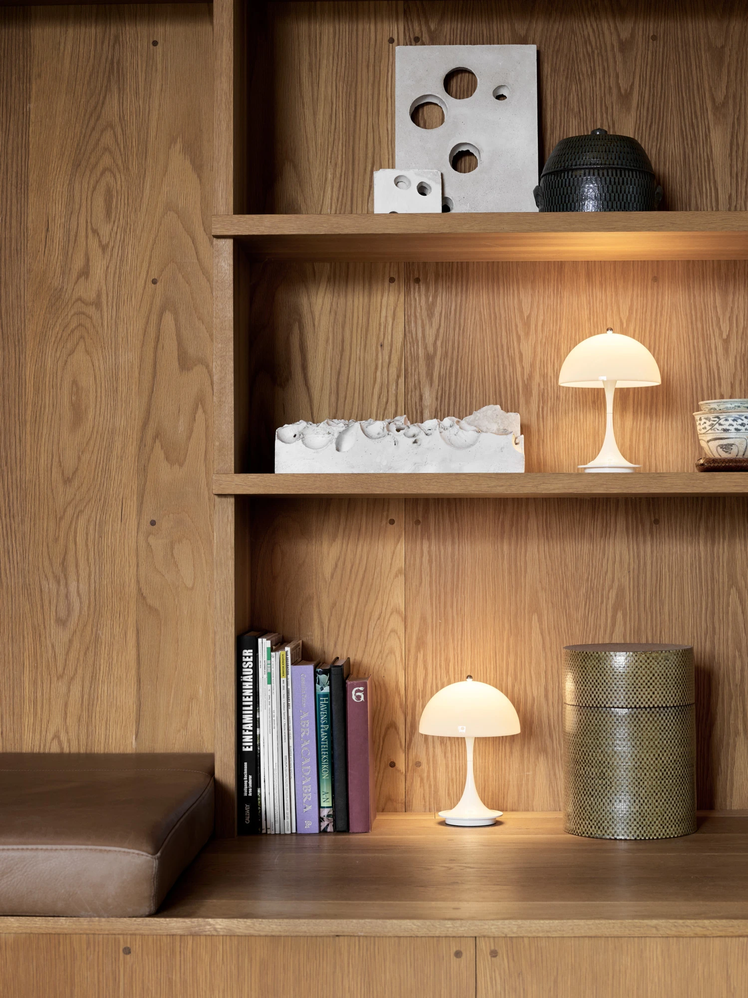 Twee witte Panthella 250 Portable Lamp tafellampen verlichten een eikenhouten kast met boeken en keramiek. © 2026 Louis Poulsen.