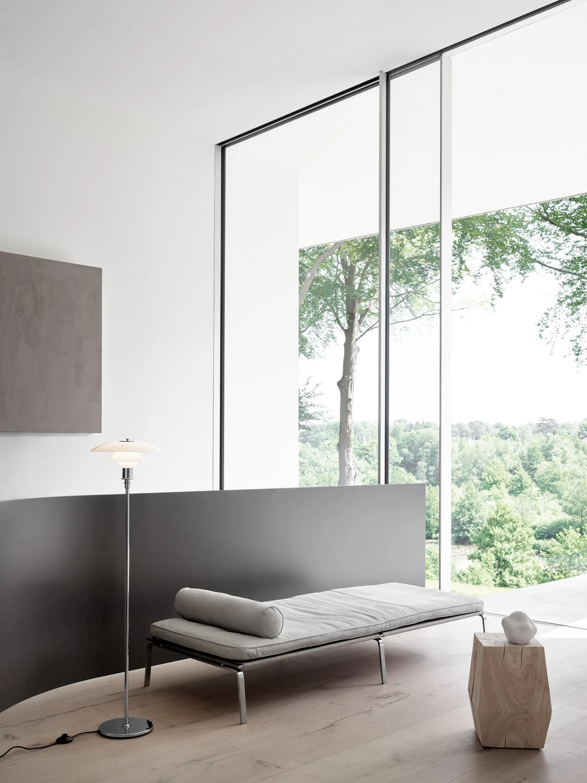 A PH 3½-2½ Floor Lamp with white shades beside a daybed in a bright room overlooking trees. © 2026 Louis Poulsen.