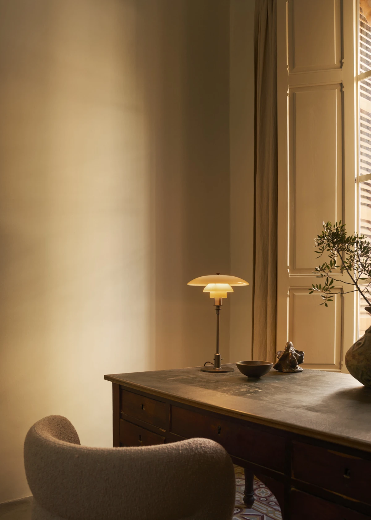 A PH 3/2 table lamp casts a warm glow across a dark desk in a classic home office. © 2026 Louis Poulsen.