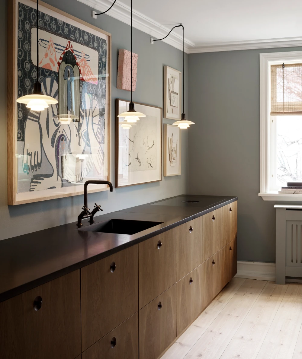 White PH 2/1 Pendants hang above a kitchen counter with a dark stone surface and wooden cabinets. © 2026 Louis Poulsen.