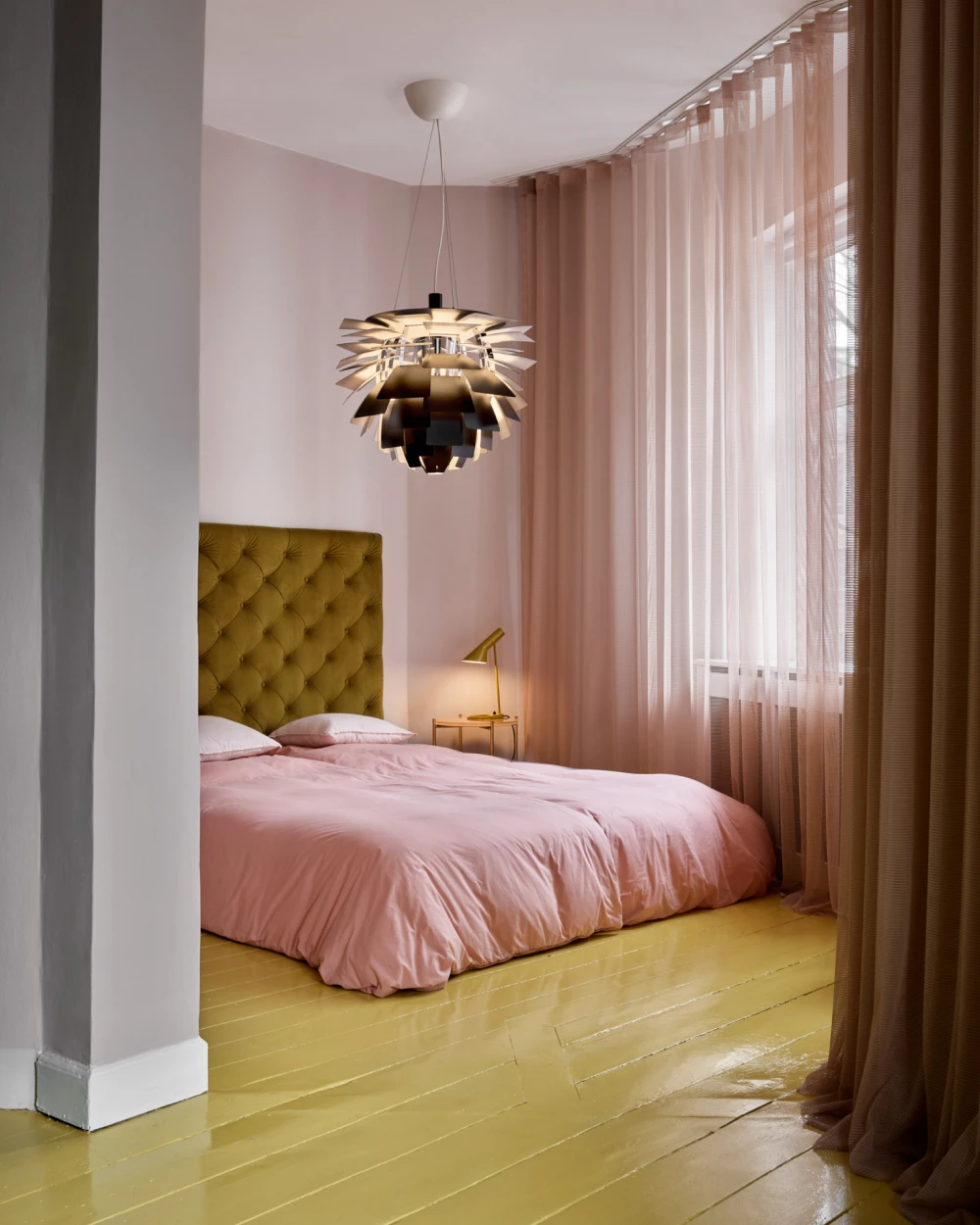 A metallic PH Artichoke pendant above a bed with pink bedding and a pale yellow wooden floor. © 2026 Louis Poulsen.