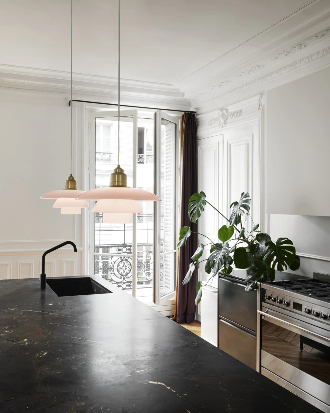 Two PH 3½-3 Pale Rose Brass Pendants hang over a dark kitchen island in a bright kitchen with classic panelling. © 2026 Louis Poulsen.