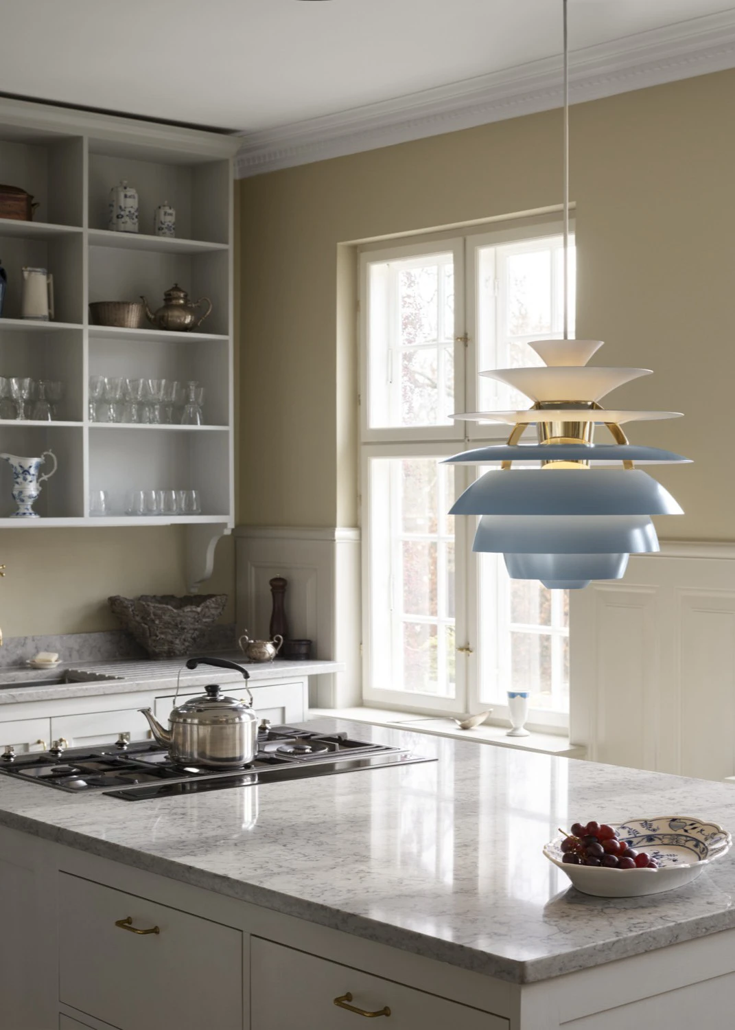 A pale blue and white PH Snowball pendant hangs above a kitchen island with a marble countertop. © 2026 Louis Poulsen.