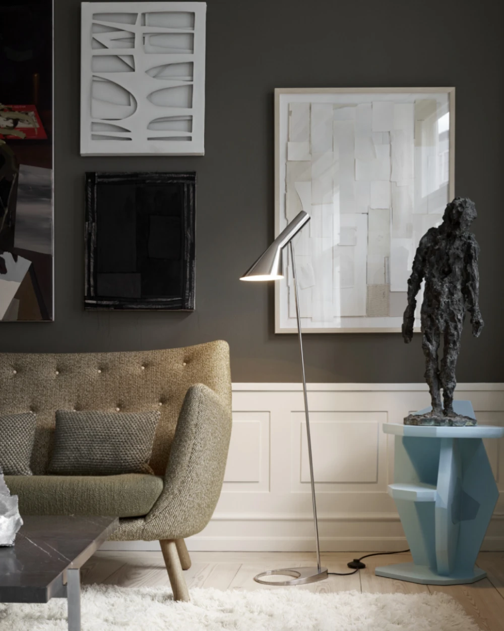 A silver AJ Floor Lamp stands beside a beige armchair in a living room with framed artwork. © 2026 Louis Poulsen.