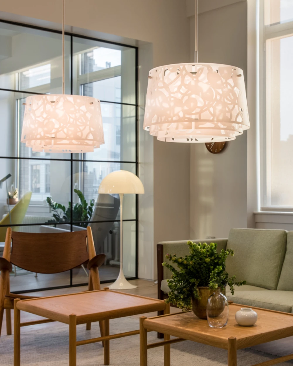 Two white LC Shutters Pendants hang over the coffee tables, with a Panthella Floor Lamp by the living room window. © 2026 Louis Poulsen.