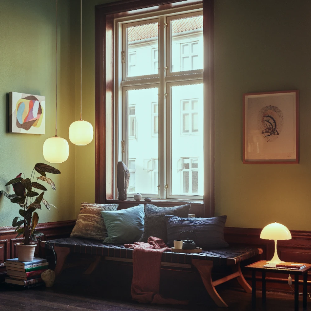 Two VL 45 Radiohus pendants and a Panthella 250 Table Lamp light a living room with green walls and wooden furniture. © 2026 Louis Poulsen.