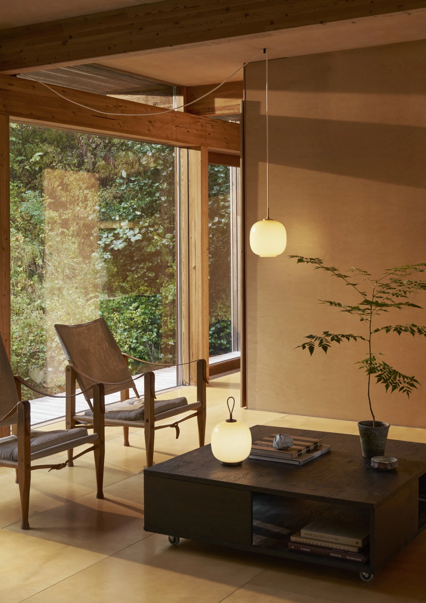 Een VL 45 Radiohus hanglamp en een draagbare VL 45 Radiohus lamp verspreiden warm licht in een woonkamer met houten balken. © 2026 Louis Poulsen.