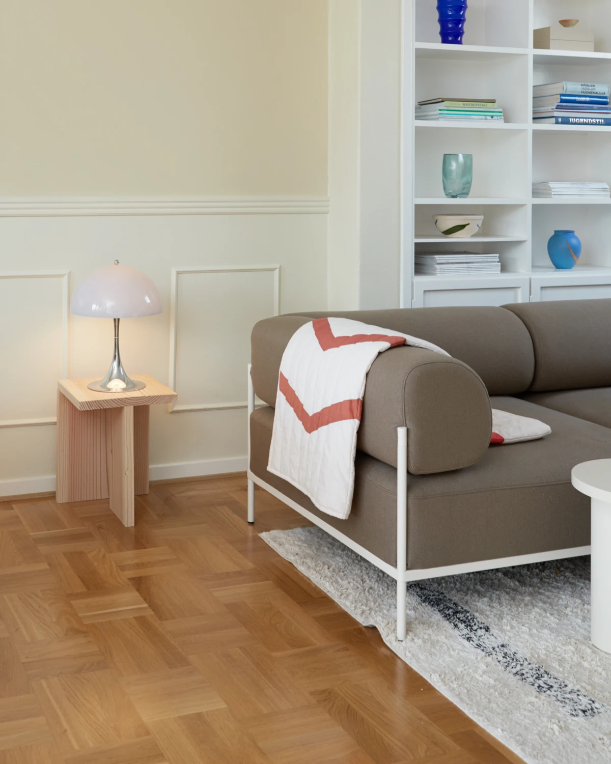 A Panthella 250 Table Lamp with a pale pink shade glows beside a sofa in a light-filled living room. © 2026 Louis Poulsen.