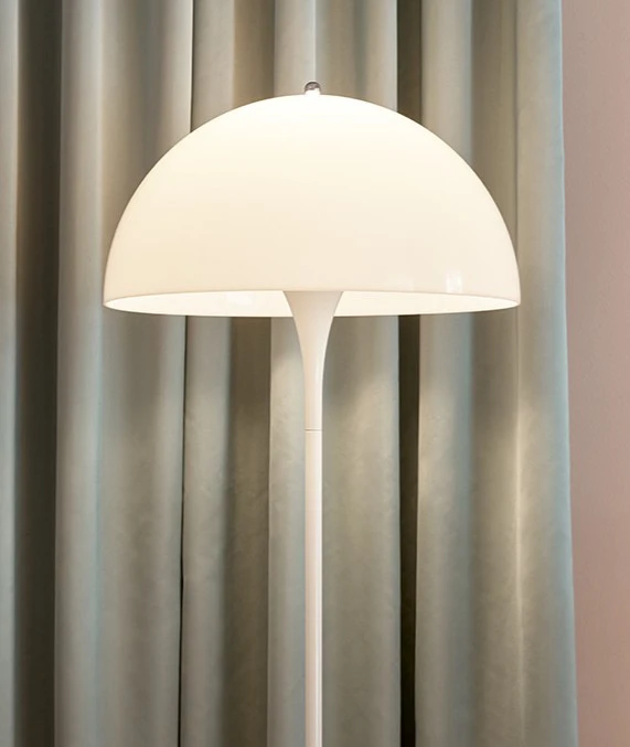 Een witte Panthella vloerlamp schijnt voor lange, grijsg beige gordijnen. © 2026 Louis Poulsen.