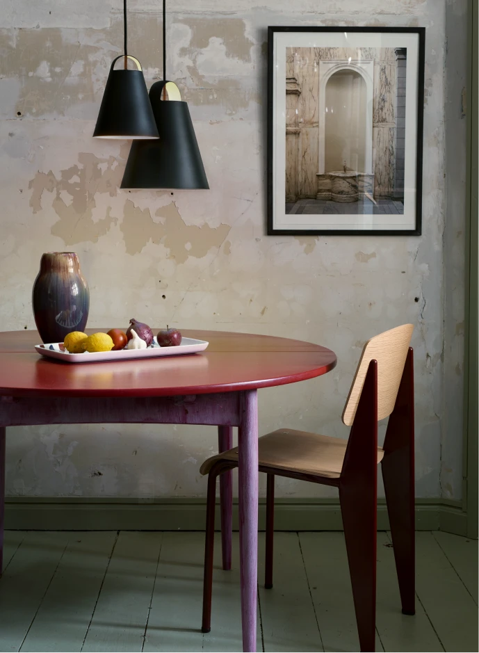 Two black Above Pendant lights hang over a red dining table against a distressed wall. © 2026 Louis Poulsen.