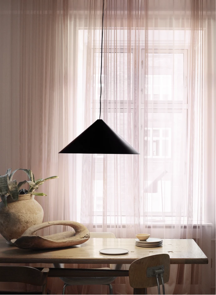 A black Keglen Pendant hangs above a wooden dining table in front of sheer curtains. © 2026 Louis Poulsen.
