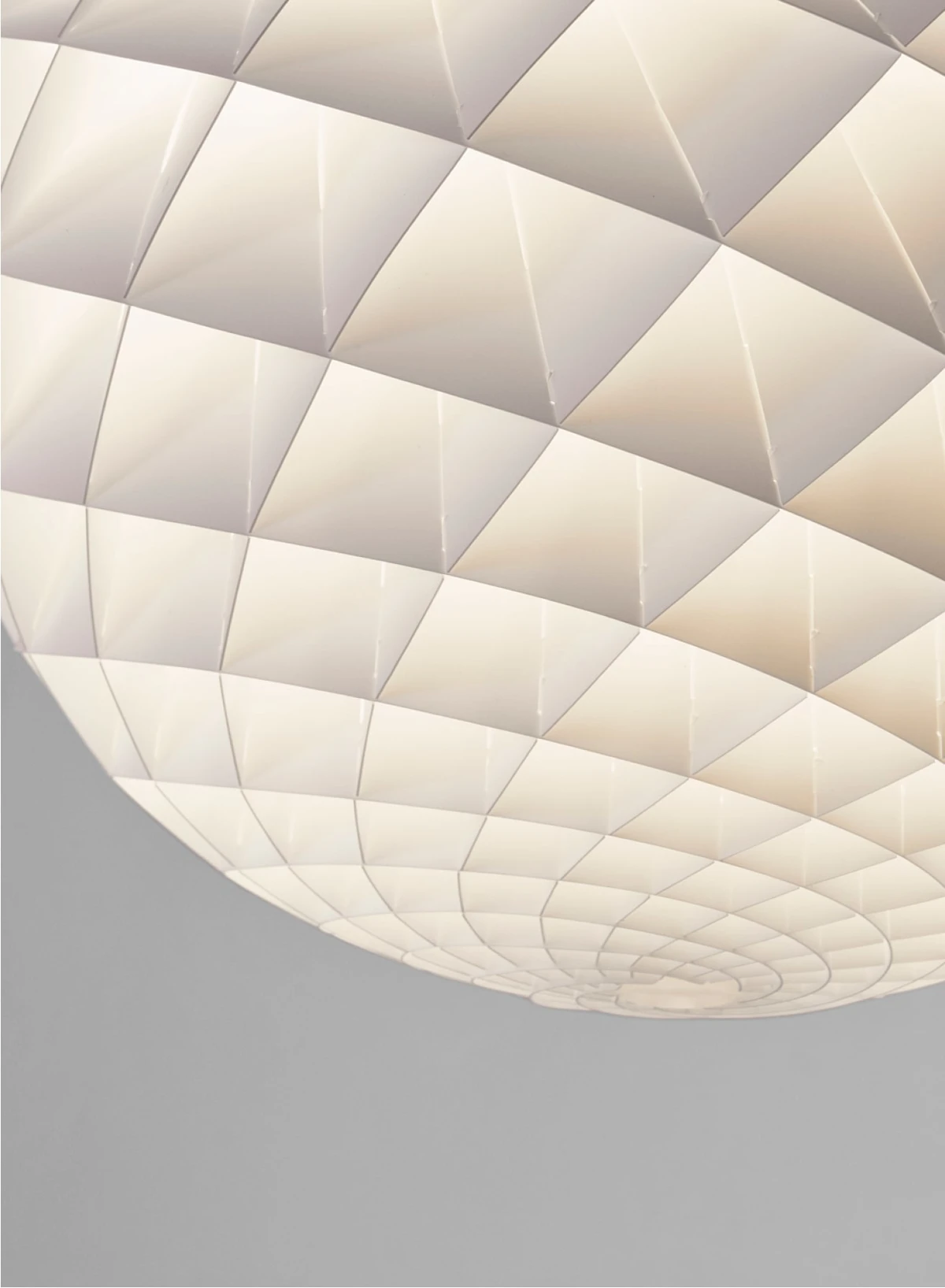 Close-up van de lichtgevende, witte Patera Pendant met een geometrisch patroon tegen een grijze achtergrond. © 2026 Louis Poulsen.