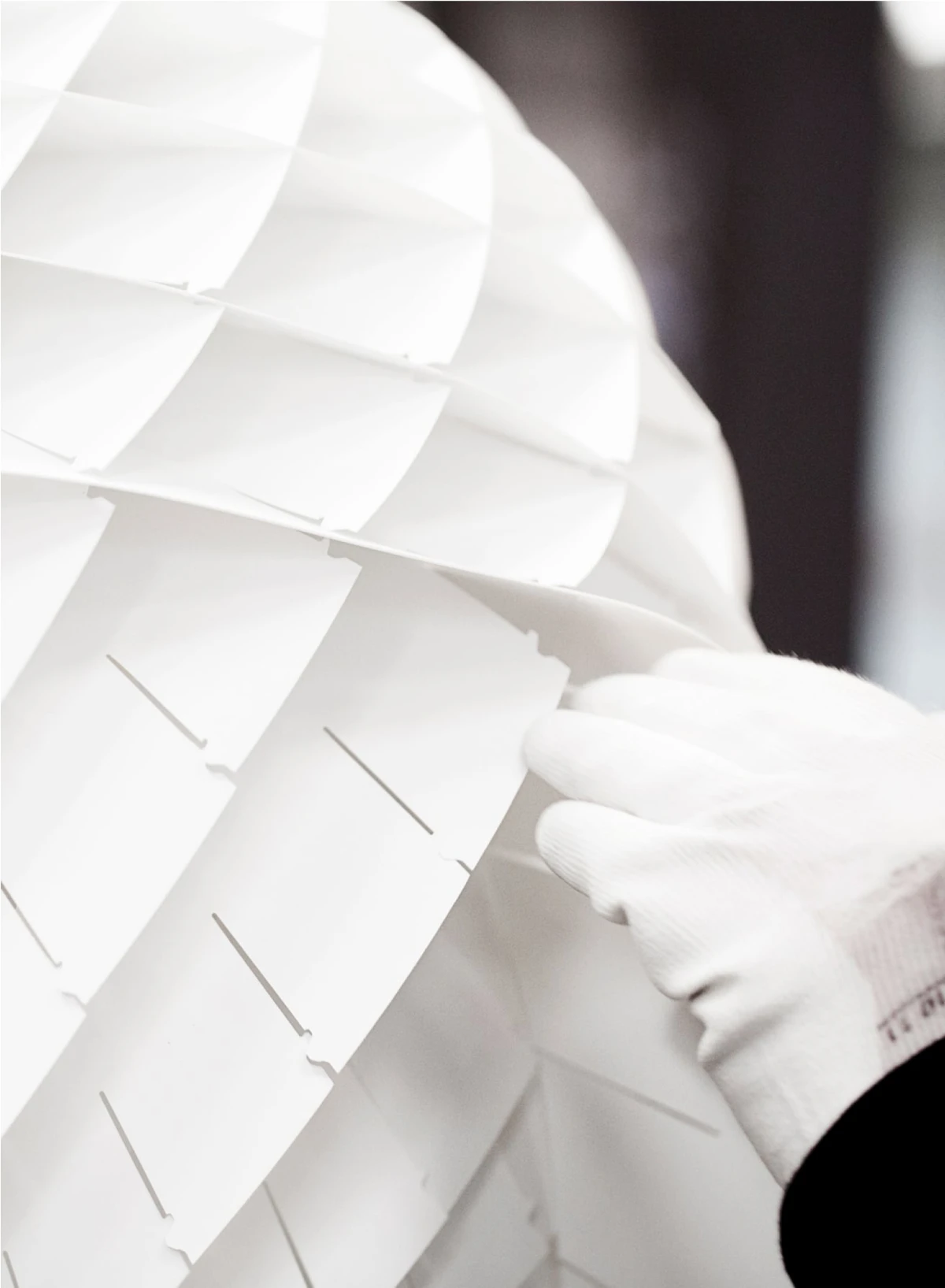 Een witte Patera hanglamp wordt met de hand gemonteerd; de overlappende, opengewerkte kappen zijn van dichtbij te zien. © 2026 Louis Poulsen.
