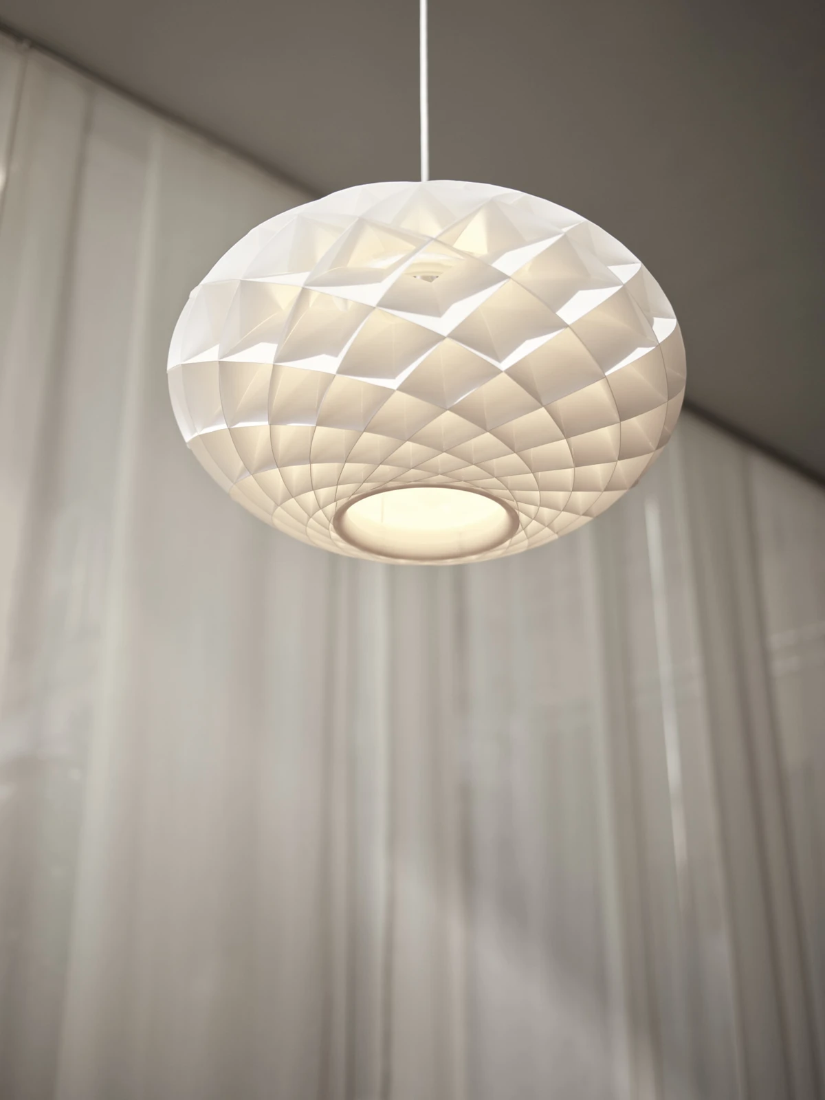 Een witte Patera Oval hanglamp verspreidt warm licht voor lichte gordijnen. © 2026 Louis Poulsen.