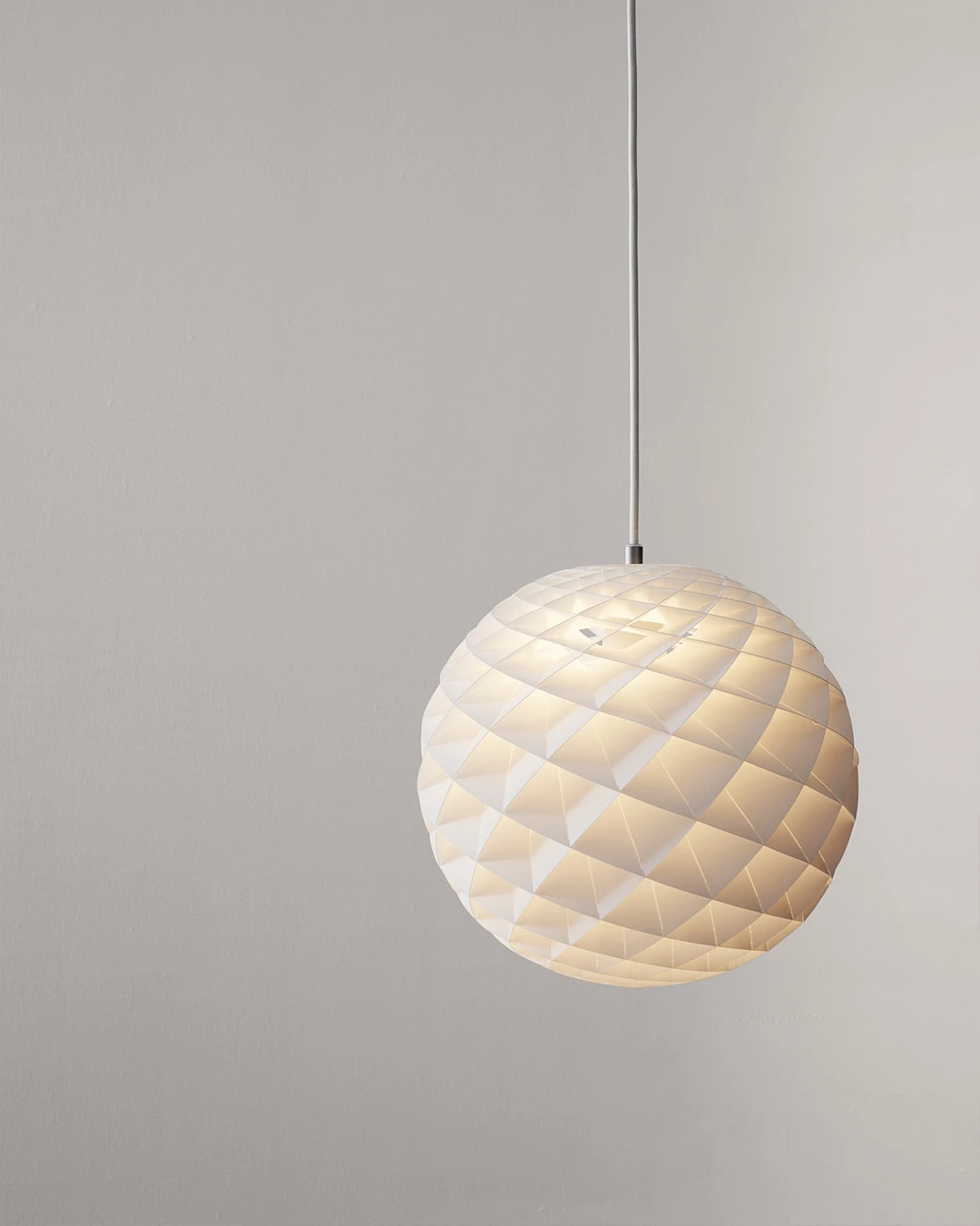 Een witte Patera hanglamp gloeit warm tegen een lichte, neutrale muur. © 2026 Louis Poulsen.