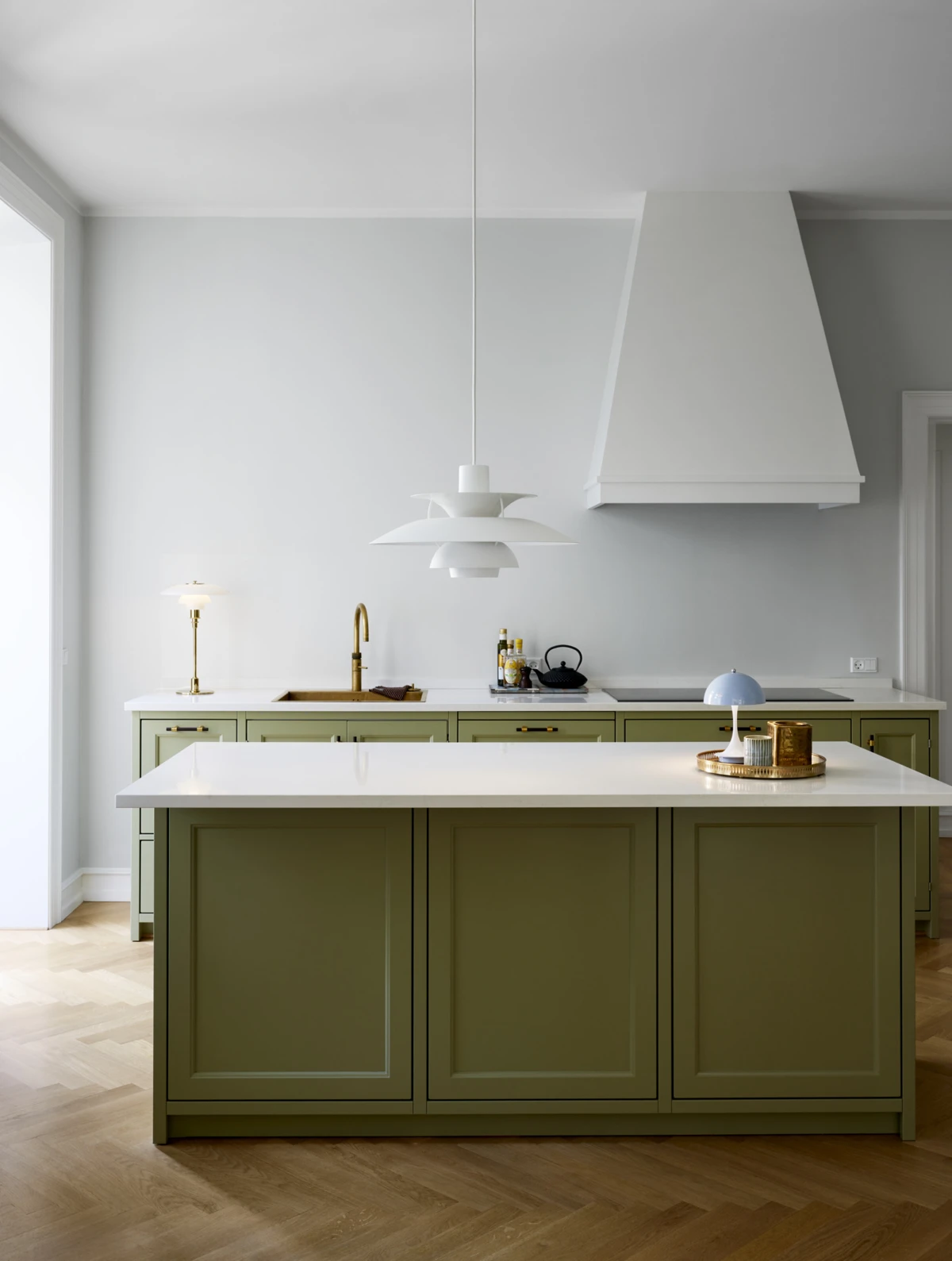 Een witte PH 5 hanglamp hangt boven het kookeiland, met een PH 3/2 tafellamp en een lichtblauwe Panthella 160 Portable Lamp. © 2026 Louis Poulsen.