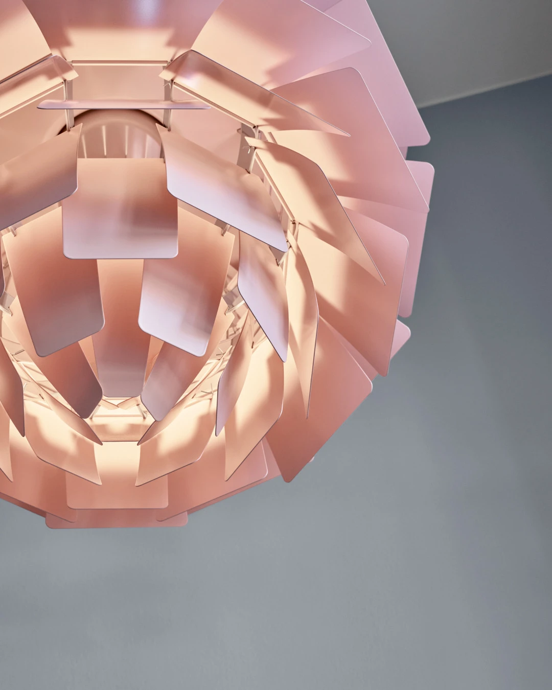 Close-up van de zachtroze PH Artichoke Pale Rose hanglamp, met gelaagde lamellen die warm oplichten tegen een grijze achtergrond. © 2026 Louis Poulsen.