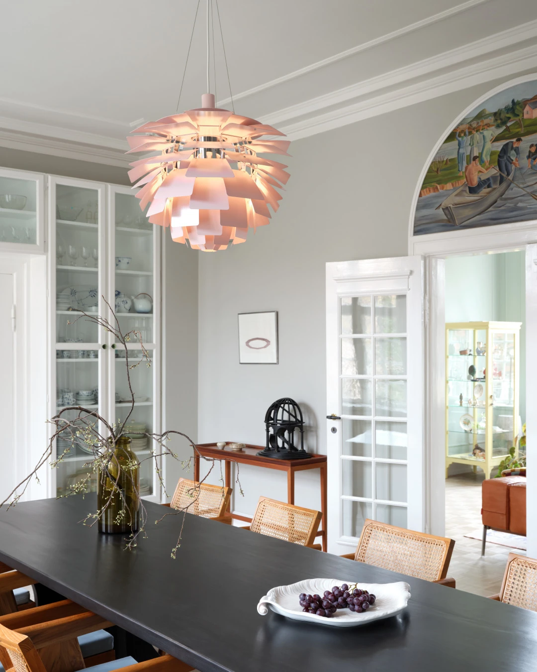 Een PH Artichoke Pale Rose hanglamp verlicht een donkere eettafel in een lichte eetkamer. © 2026 Louis Poulsen.
